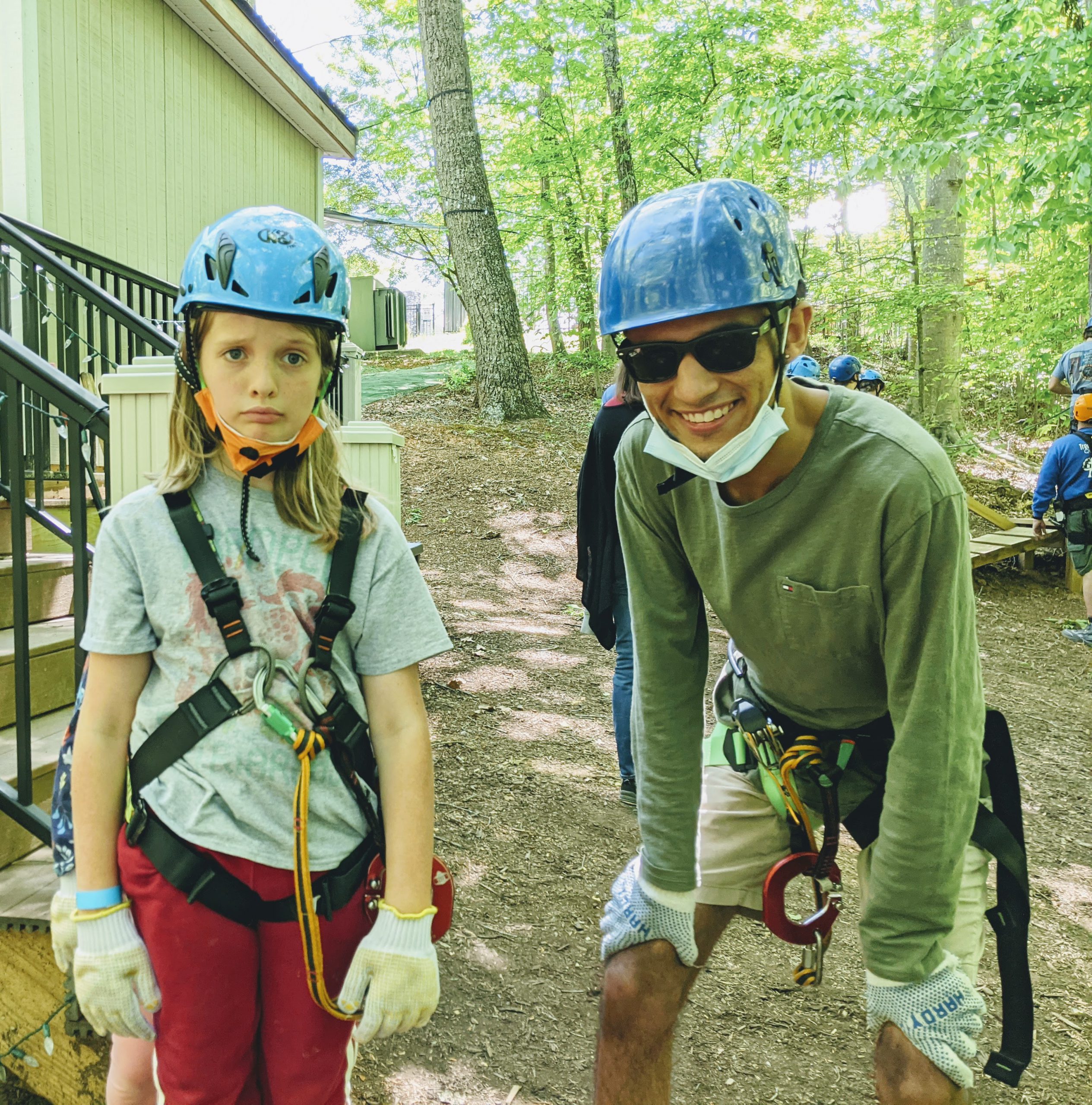 Carlos, grinning, with Silas, looking distressed, both wearing their high ropes gear--harnesses, gloves, helmets.