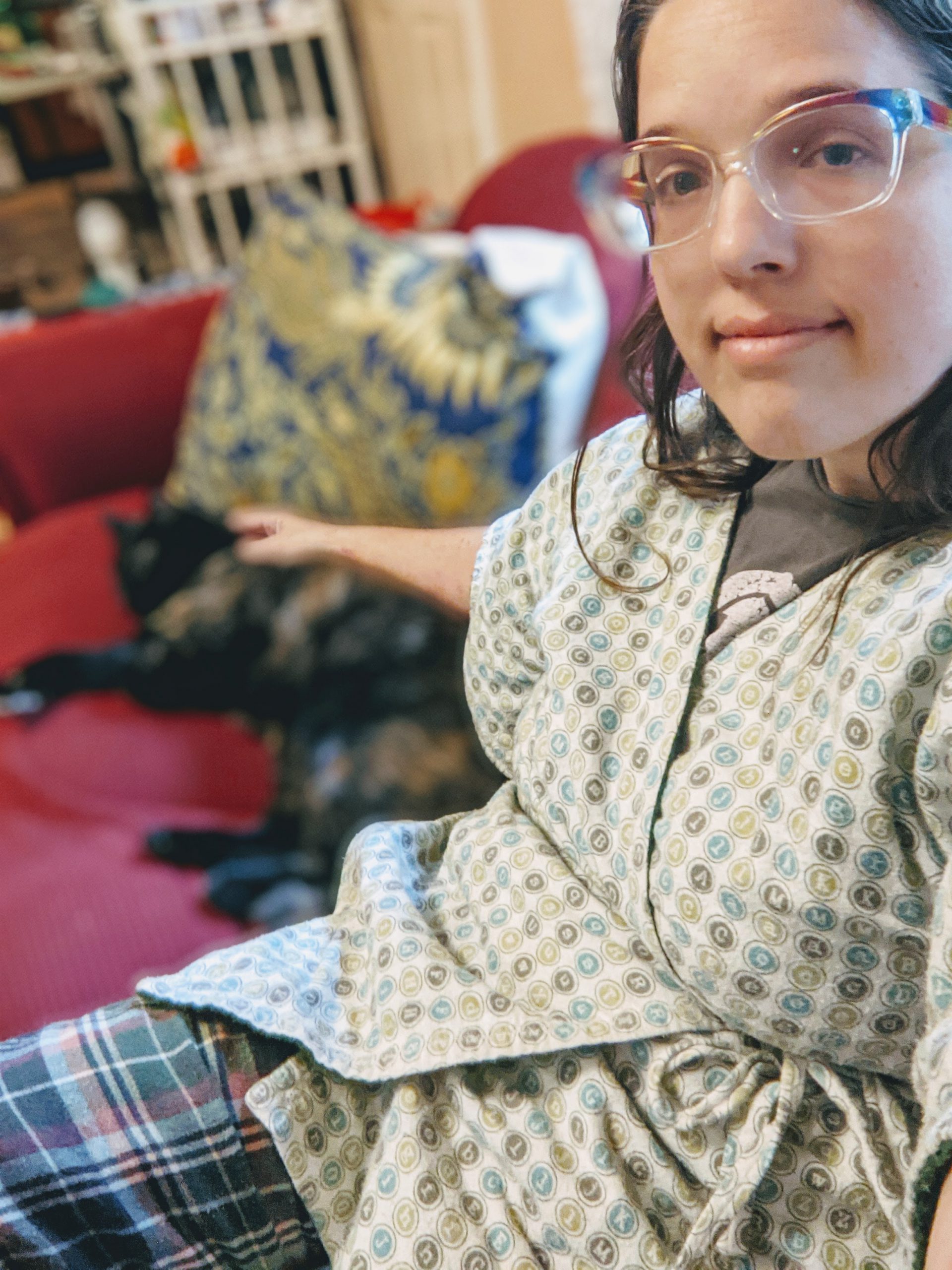 Aili in pajamas with short flannel robe. The robe is printed all over with typewriter keys. Her cat Clementine is in the background.