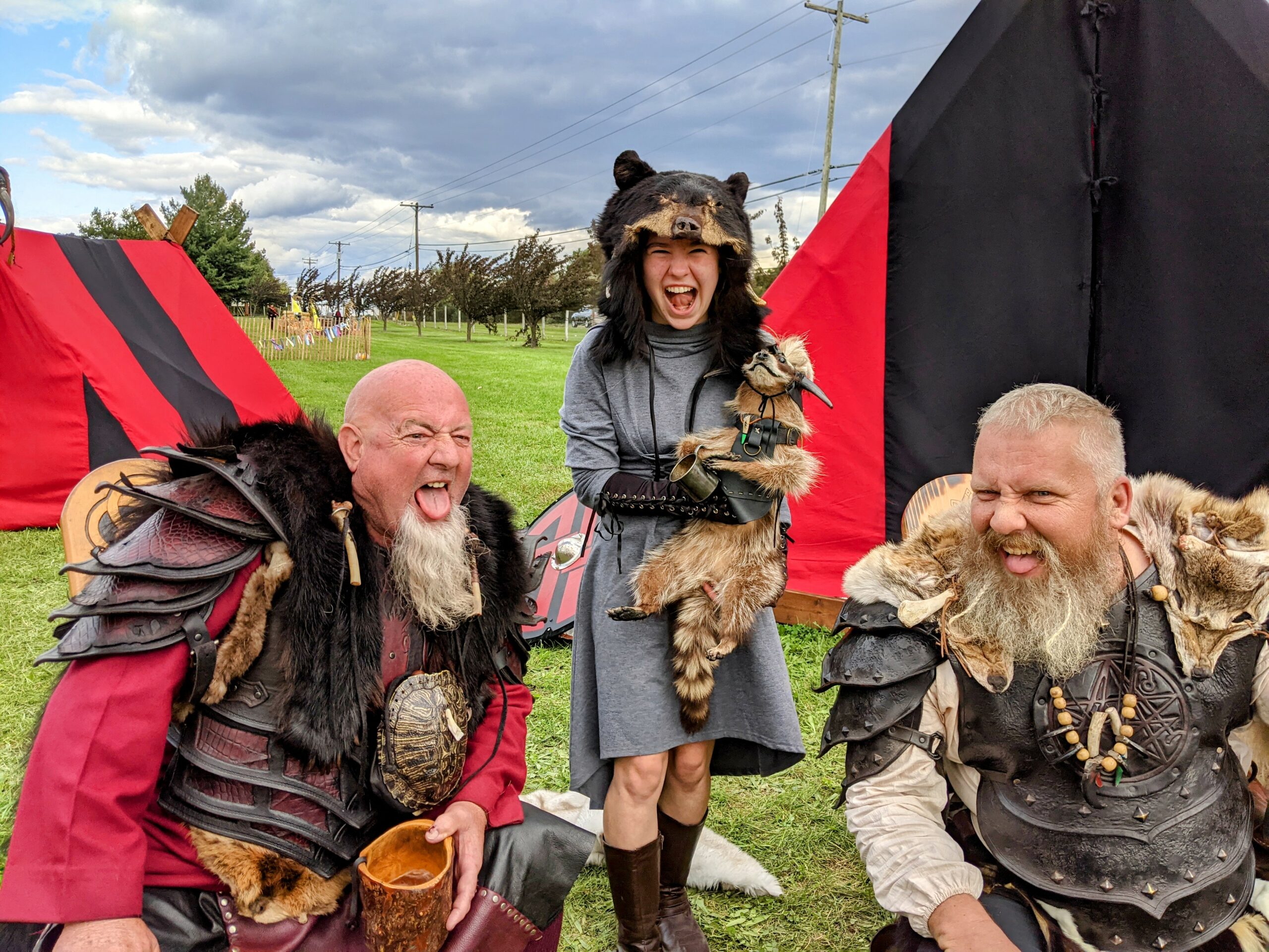 Lillian wearing a bear head, holding a raccoon, and making a fierce face with two men dressed as barbarians.