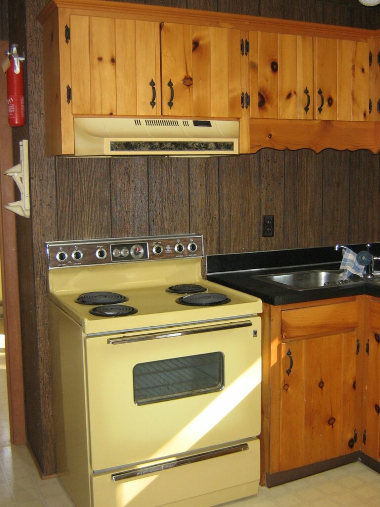 "Before" picture of the kitchen: Pine cabinets, brown Masonite walls, avocado colored stove.