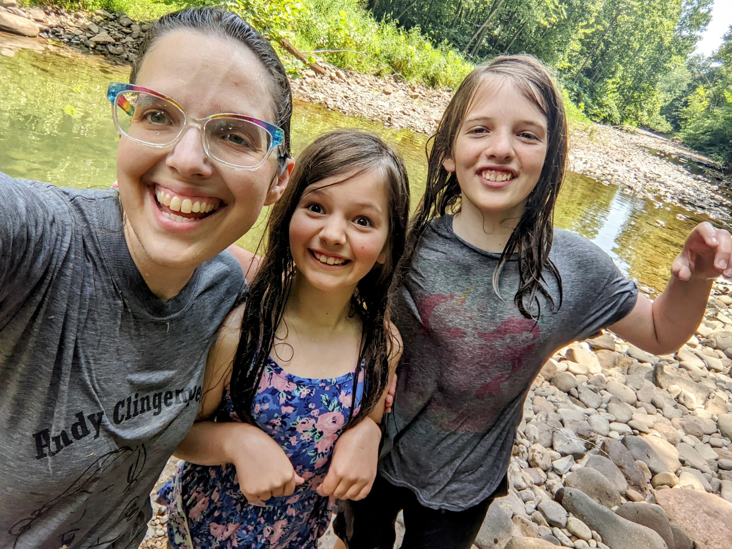 Aili, Petra, and Silas standing by the river. They're all soaking wet because they just went for a quick dunk.