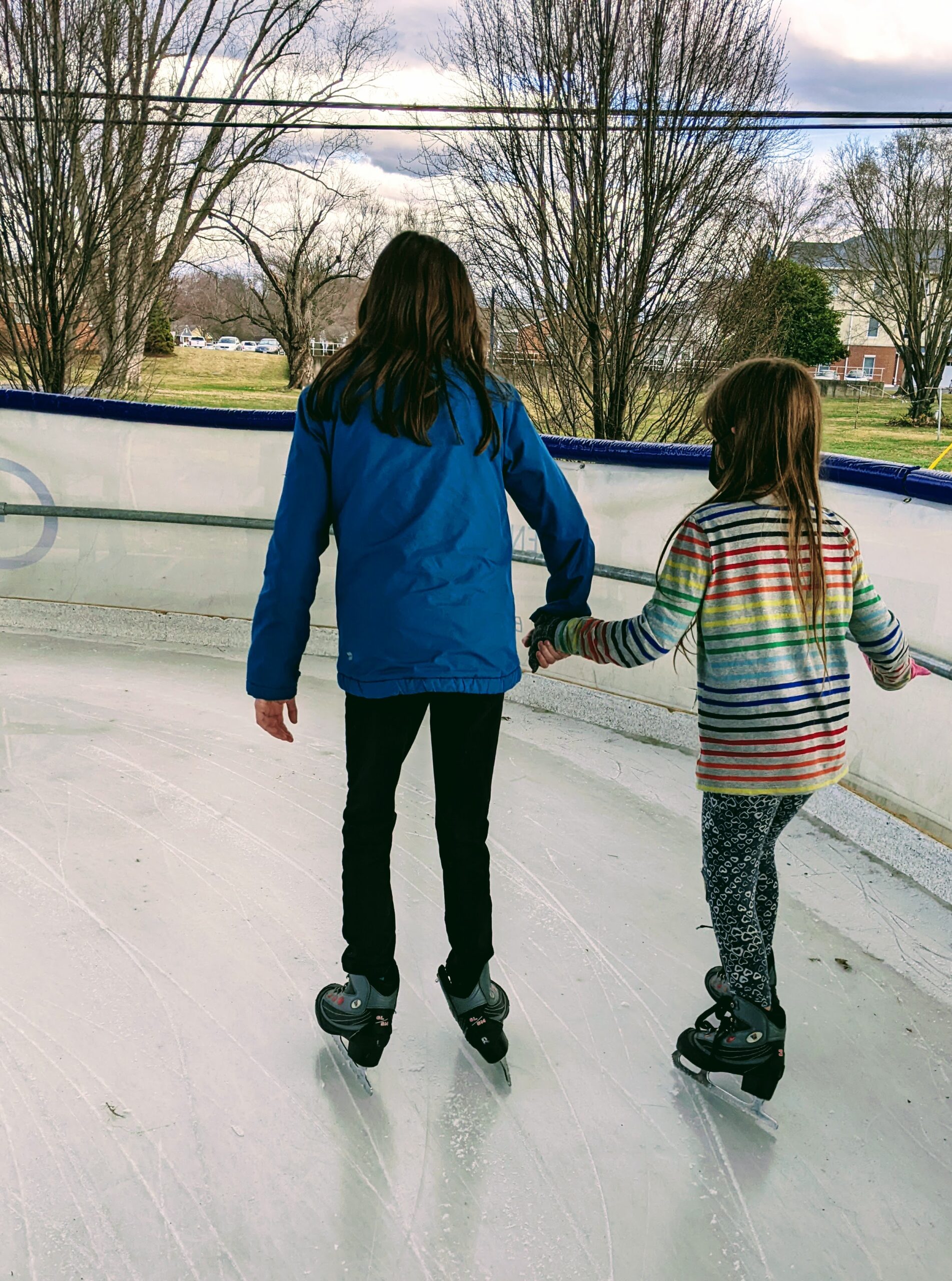Photo of Emmy and Petra ice skating, taken from behind. They are holding hands.