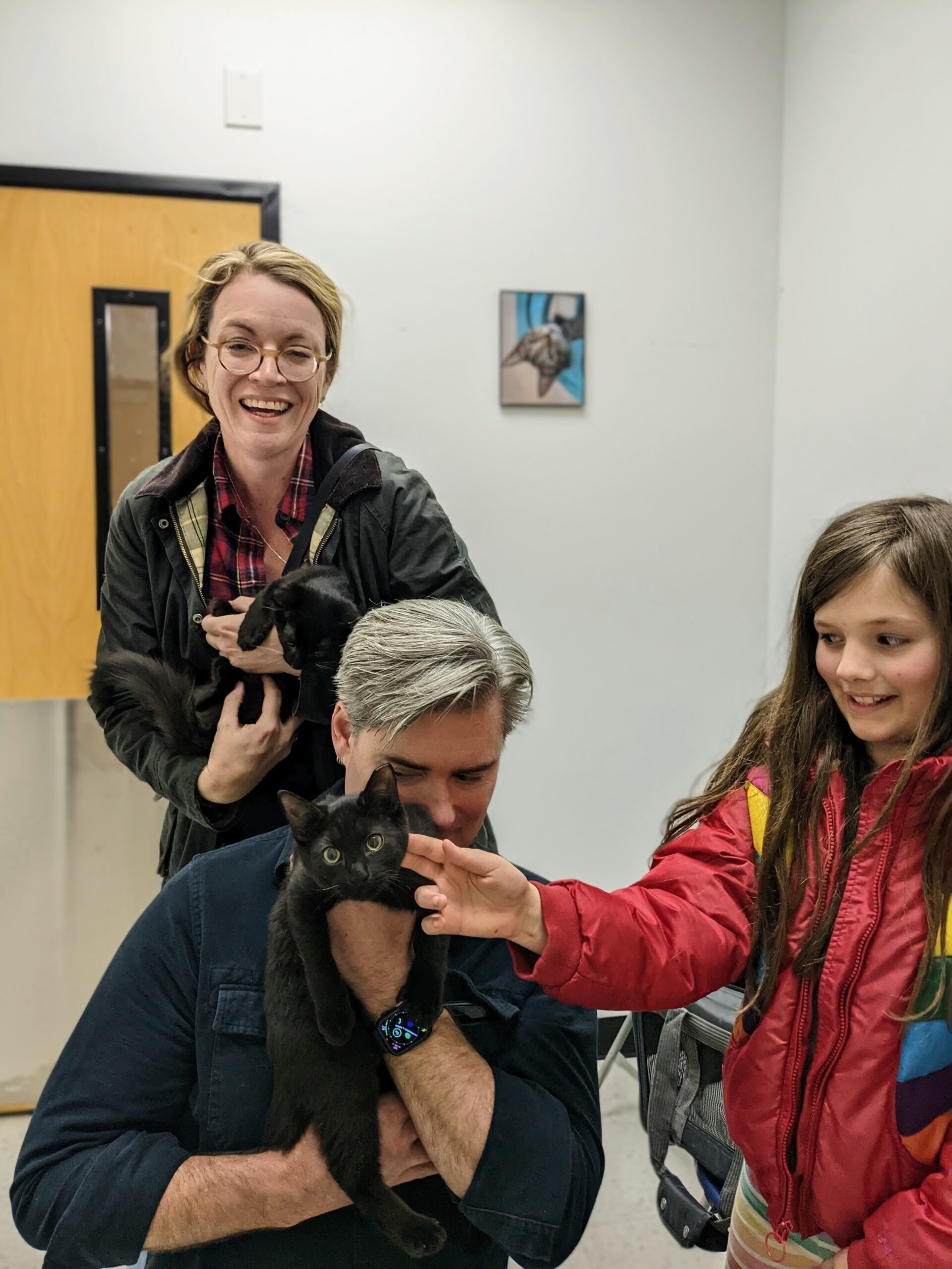 Two laughing adults hold cats, while Petra pets one of them.