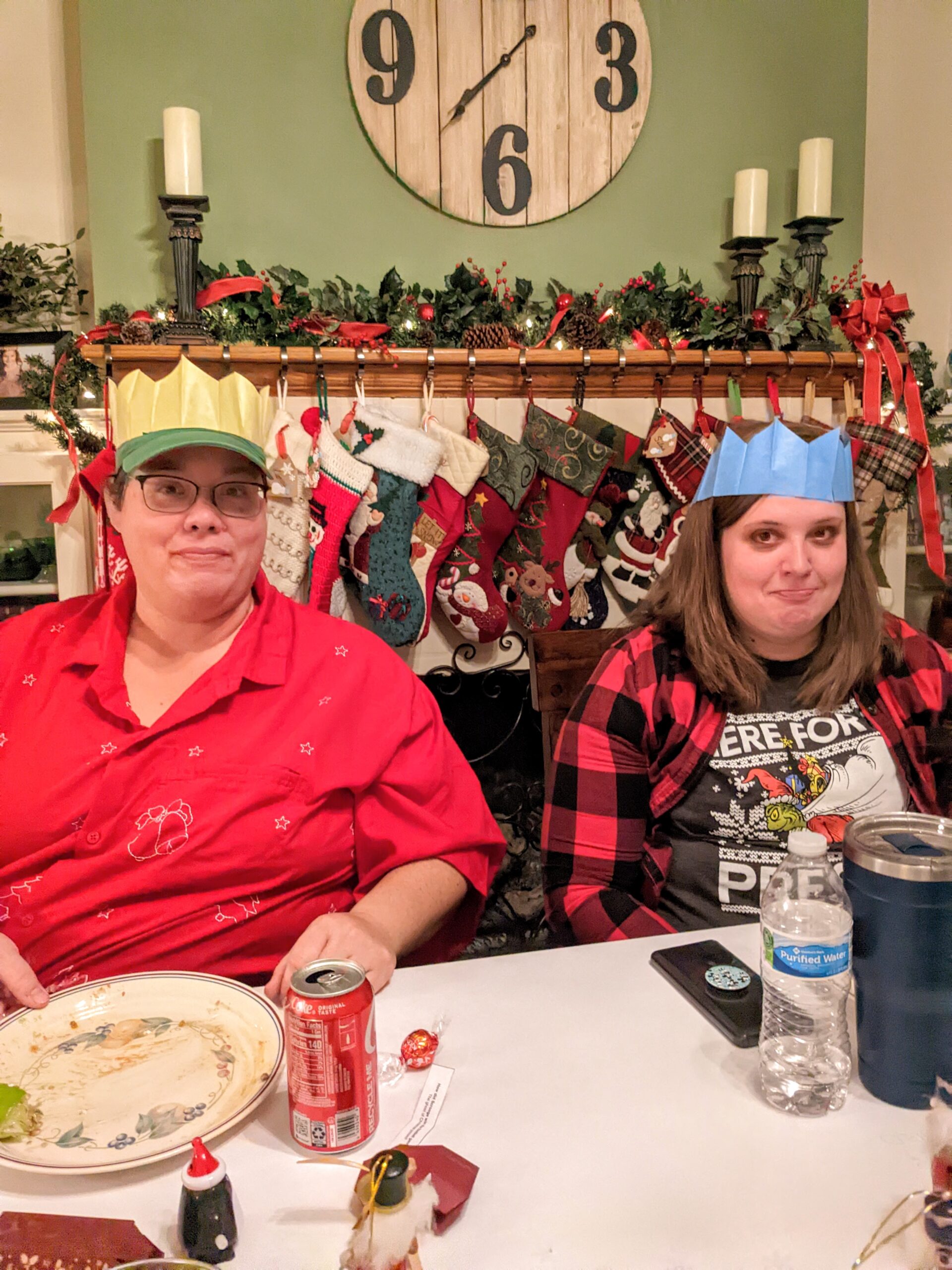 Konni and Kassi wearing paper crowns sitting at the table in front of a row of Christmas stockings.