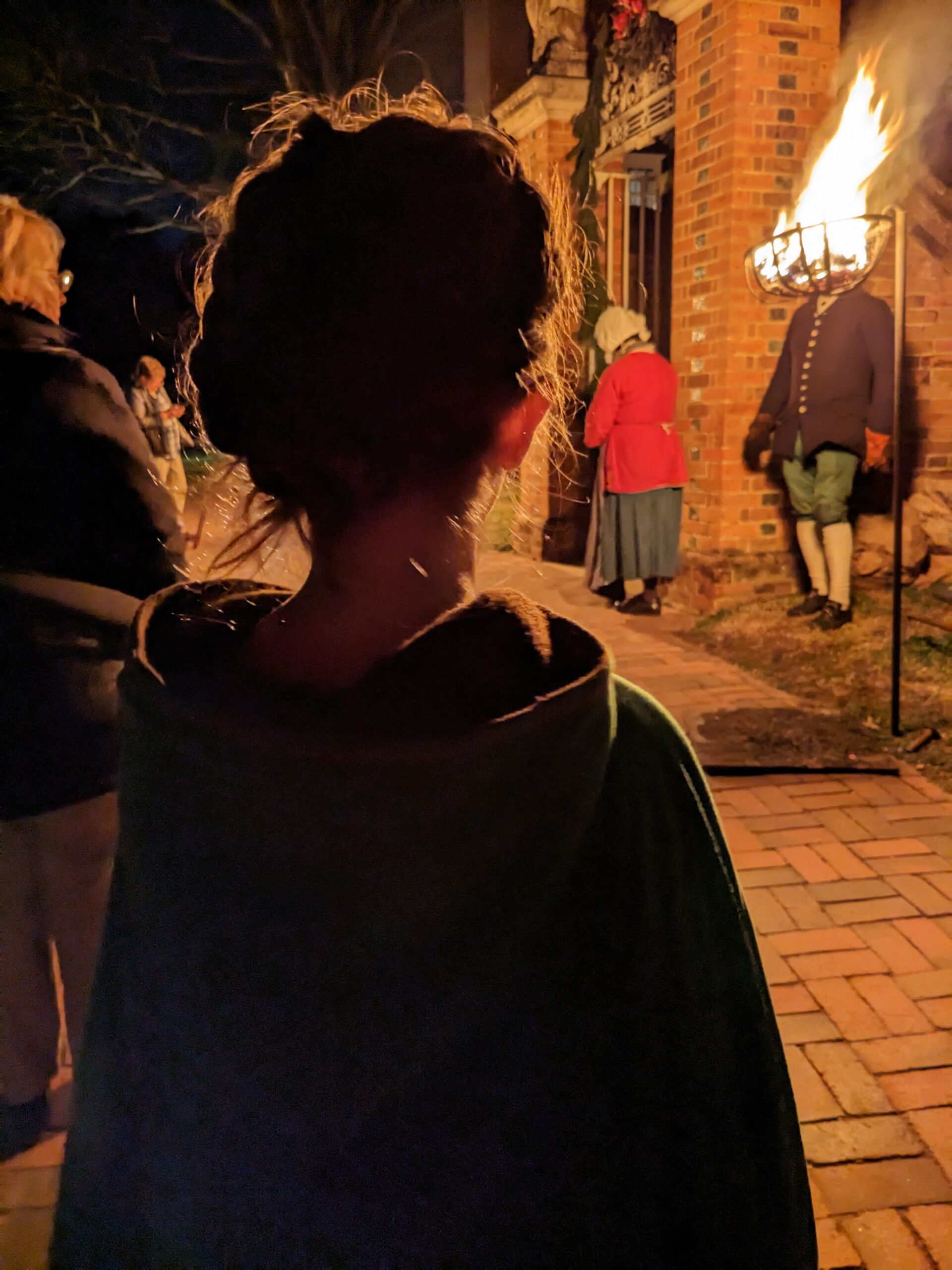 Petra, from the back, in the foreground. In the background, a flaming creosote is between the camera and a man's head.