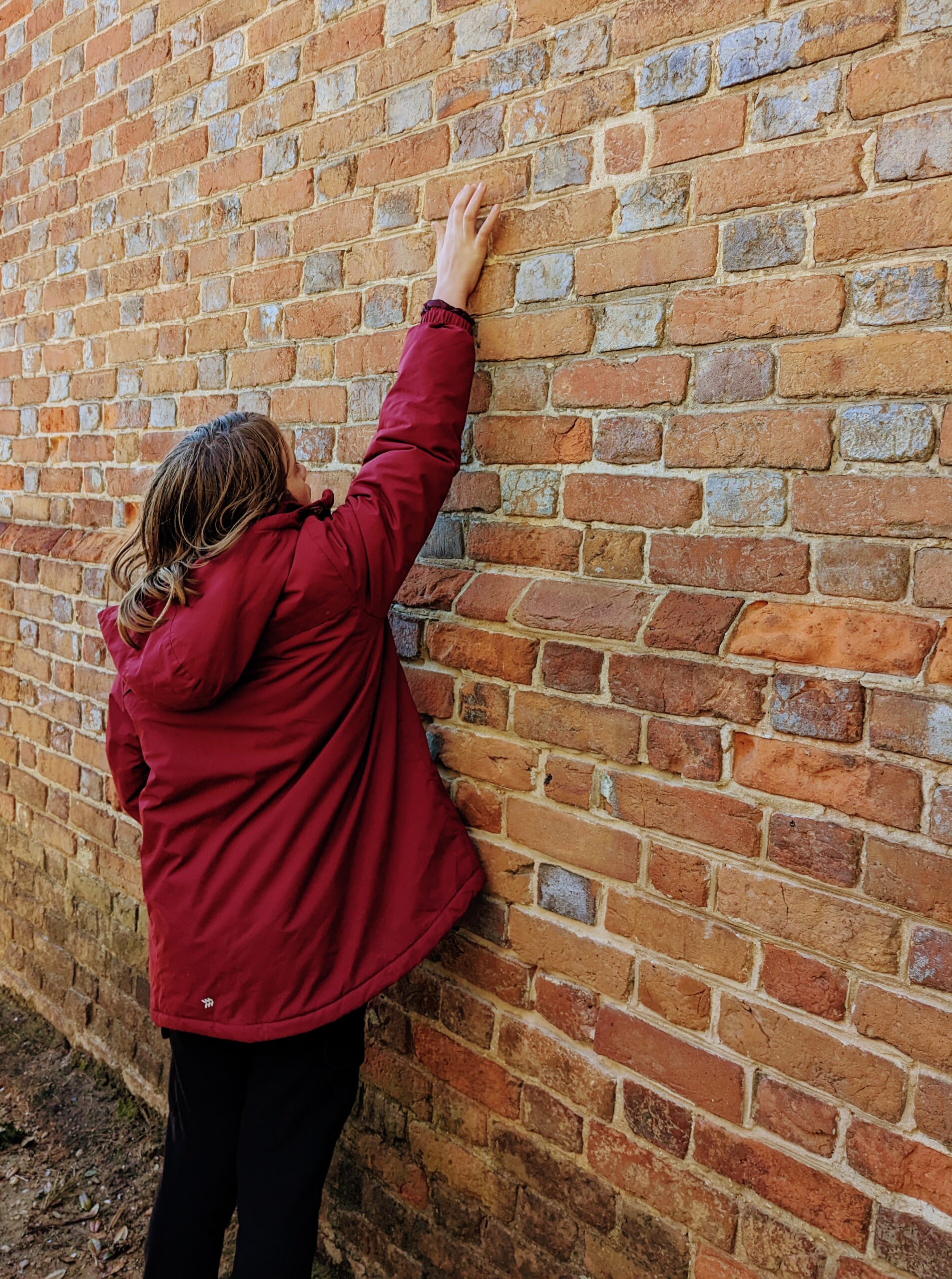 Silas reaches up a wall and fits his fingertips into the impressions left by the enslaved people who made the bricks.
