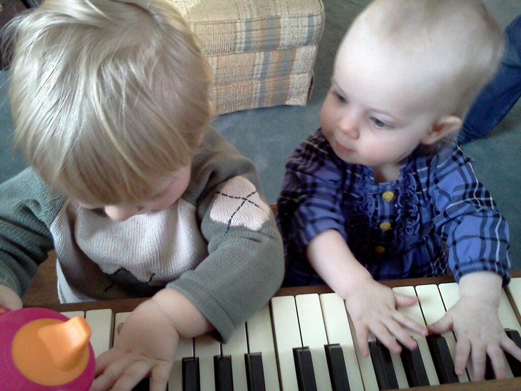 An overhead view of two toddlers, Silas and Persephone, playing a piano.