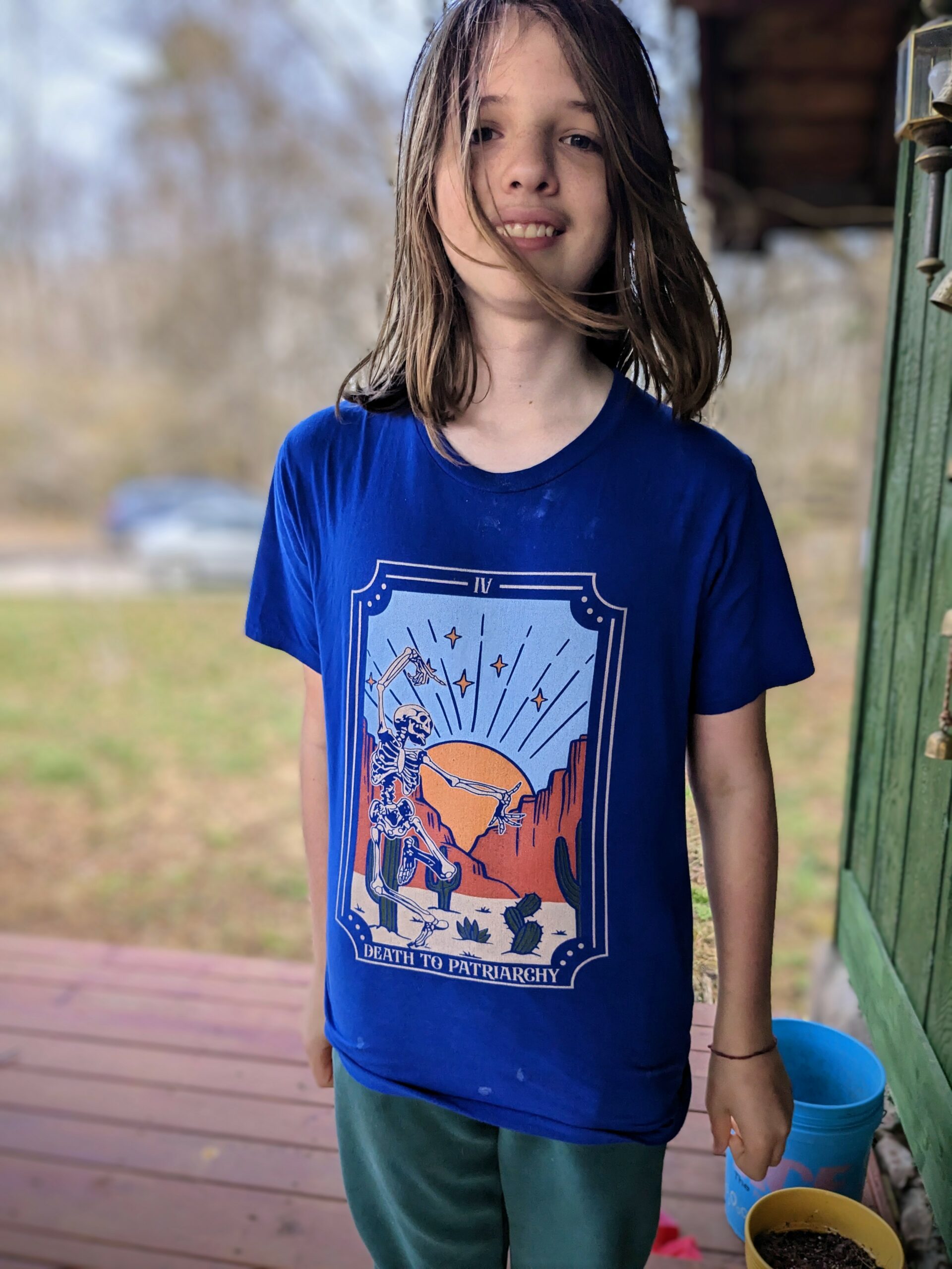 Silas, standing on the porch, wearing a shirt that looks like the Death tarot card, with the caption "Death to Patriarchy"