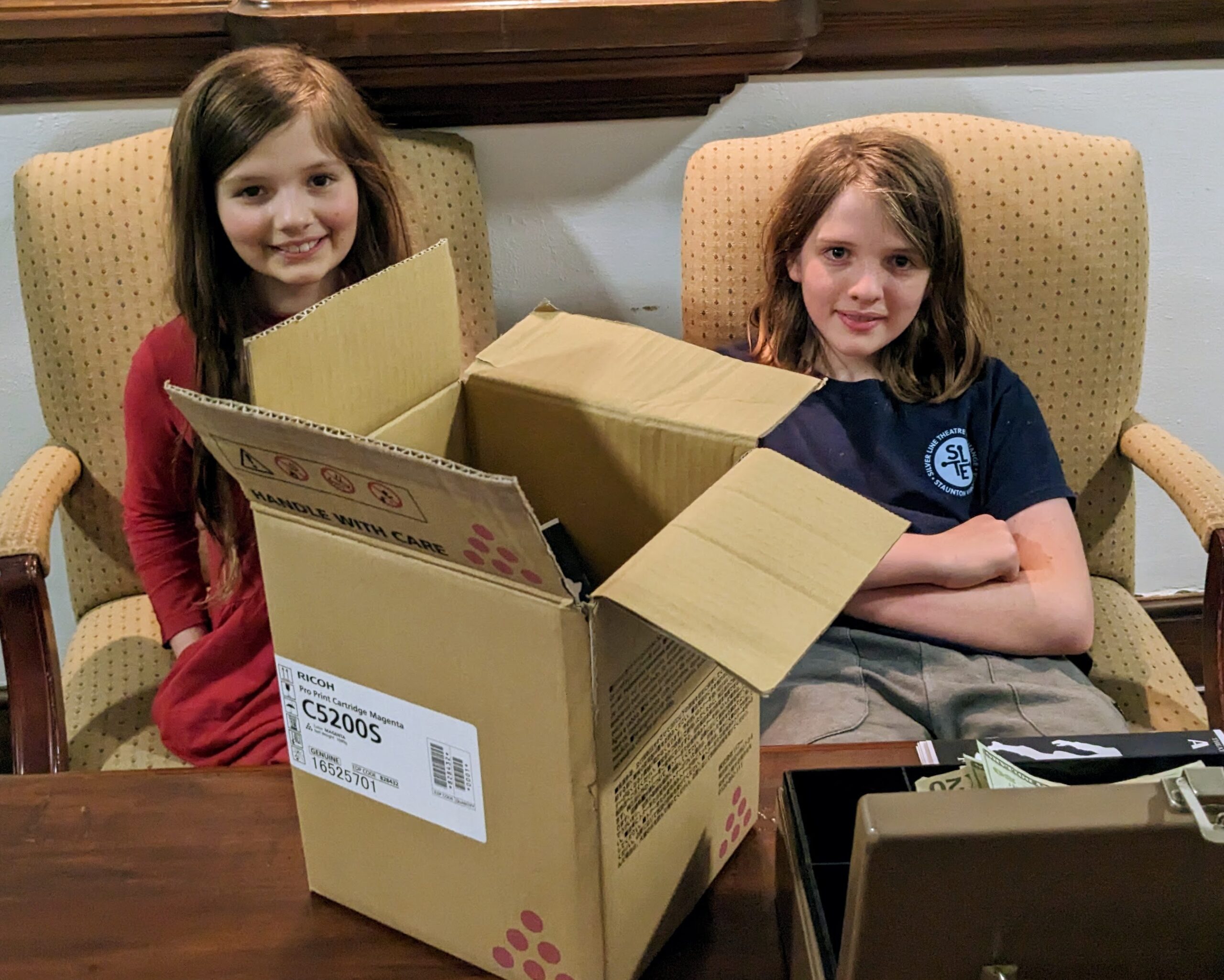 Petra and Silas sitting behind a table with a box of programs and a box of money in front of them.