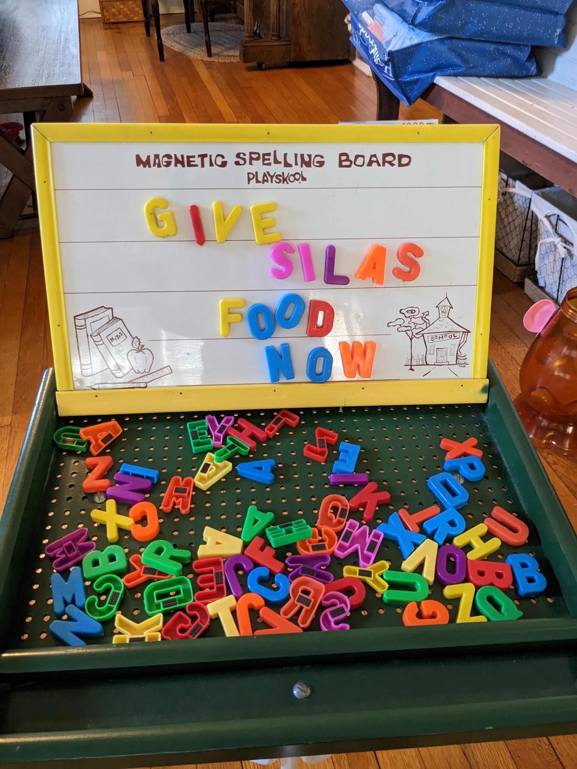 A children's magnet letter board, with the message "GIVE SILAS FOOD NOW" spelled out on it.